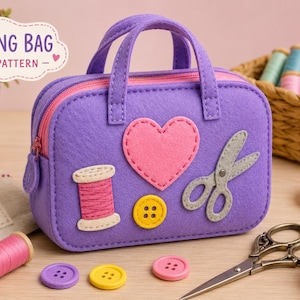 Pode incluir: Uma bolsa de costura de feltro roxa com aplicações de um coração rosa, um carretel de linha, um botão amarelo e uma tesoura cinza. A bolsa tem um zíper rosa e duas alças. O texto SEWING BAG FELT PATTERN é visível. Acessórios de costura próximos.