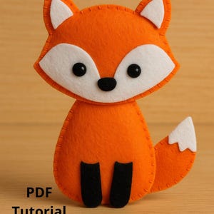 May include: An orange felt fox with white accents and black details. The fox has a white-tipped tail, white inner ears, and black eyes and feet. The text "Instant Download" and "PDF Tutorial + Pattern" are visible.