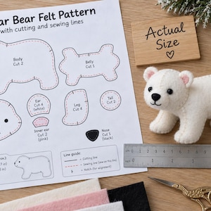 Pode incluir: Um projeto de artesanato de urso polar em feltro com uma folha de molde impressa com linhas de corte e costura, um urso polar de feltro acabado, uma régua metálica de 15 cm, tesoura e retalhos de feltro nas cores branca, rosa e preta.