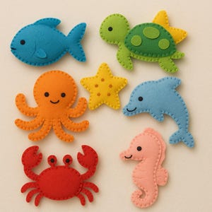 Pode incluir: Uma coleção de criaturas marinhas de feltro, incluindo um peixe azul, uma tartaruga verde, um polvo laranja, uma estrela do mar amarela, um golfinho azul, um caranguejo vermelho e um cavalo-marinho rosa. Cada criatura é costurada à mão.