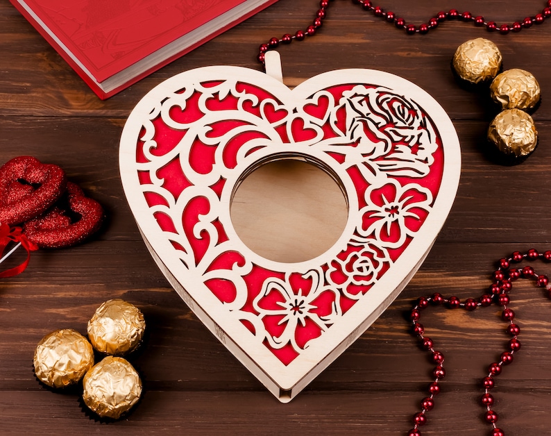 May include: A wooden heart-shaped box with a cutout design. The box is painted red and has a floral pattern. The box is open and empty.