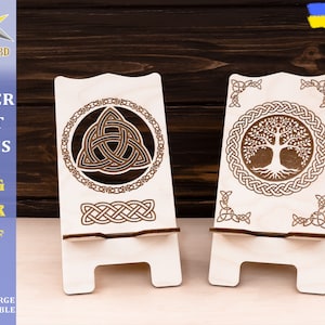 May include: Two wooden phone stands with intricate Celtic knot designs. One stand features a triquetra knot, while the other has a tree of life design.