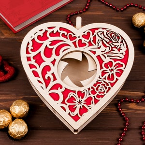 May include: A wooden heart-shaped box with a red and white floral design. The box has a cutout in the center and is perfect for holding small gifts or trinkets.