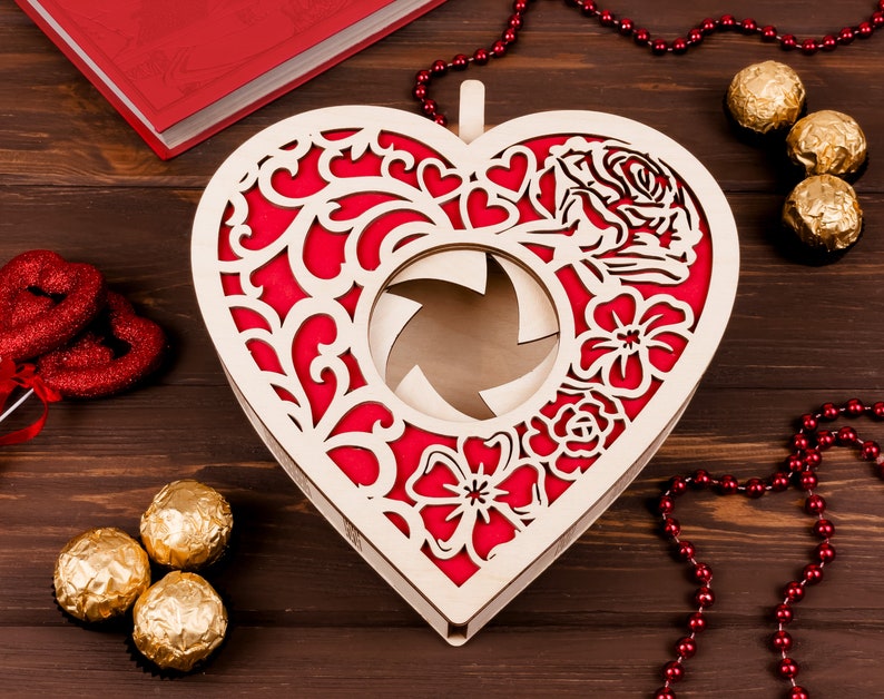 May include: A wooden heart-shaped box with a red and white floral design. The box has a cutout in the center and is perfect for holding small gifts or trinkets.