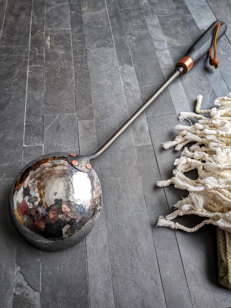 Peut inclure: Louche en m&eacute;tal martel&eacute; avec un long manche et une poign&eacute;e en bois sombre. Le bol rond et r&eacute;fl&eacute;chissant est fix&eacute; au manche par des rivets en cuivre. Une boucle en cuir est attach&eacute;e &agrave; l'extr&eacute;mit&eacute; de la poign&eacute;e.