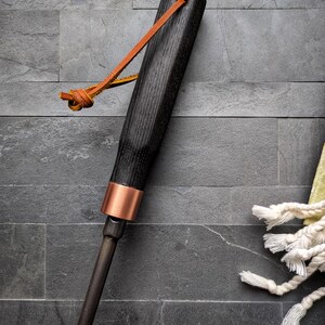 Peut inclure: Un tisonnier de chemin&eacute;e en bois noir avec une bande de cuivre et une boucle en cuir. Le tisonnier a une finition sombre et un design simple et &eacute;l&eacute;gant. La boucle en cuir est de couleur marron clair.