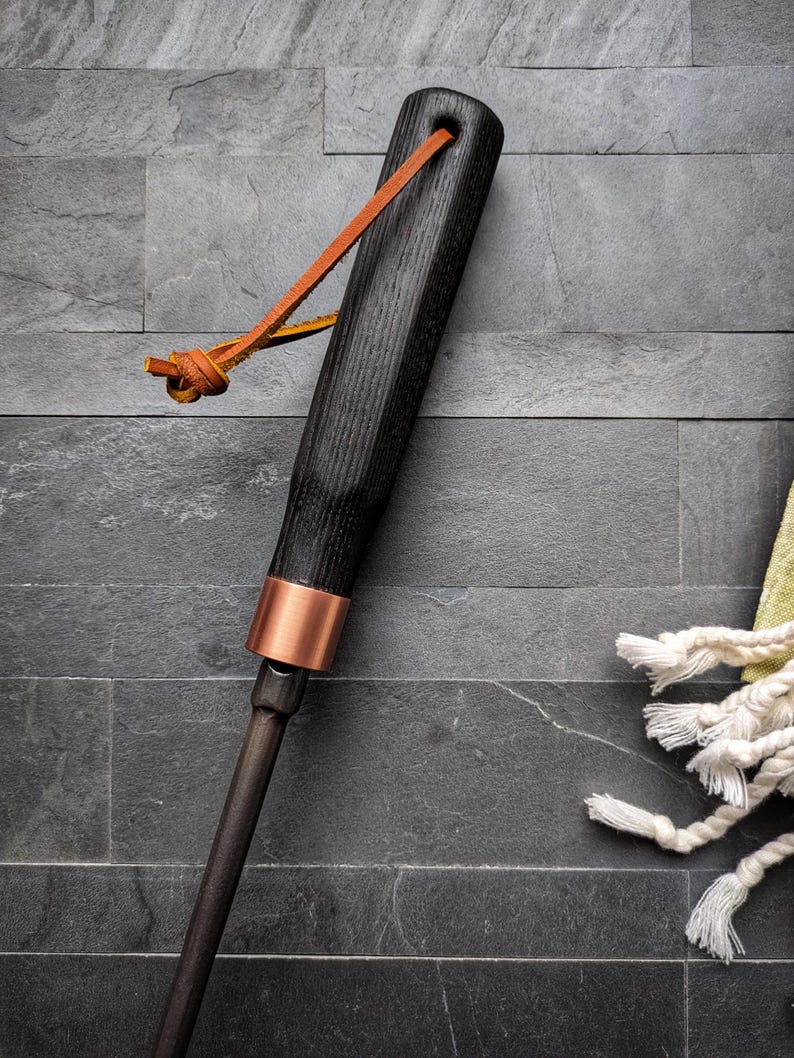 Peut inclure: Un tisonnier de chemin&eacute;e en bois noir avec une bande de cuivre et une boucle en cuir. Le tisonnier a une finition sombre et un design simple et &eacute;l&eacute;gant. La boucle en cuir est de couleur marron clair.