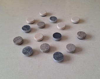 May include: A collection of small, round magnets in various shades of gray and beige. The magnets have a flat, circular shape and a textured surface, with some displaying a marbled pattern. They are arranged on a light-colored surface.