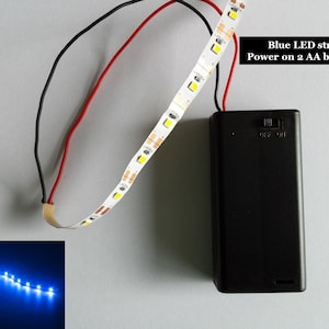 Könnte beinhalten: Ein blauer LED-Lichtstreifen mit einem Batteriefach und einem Ein-/Ausschalter. Der Lichtstreifen wird mit zwei AA-Batterien betrieben. Der Text auf dem Batteriefach lautet "OFF ON".