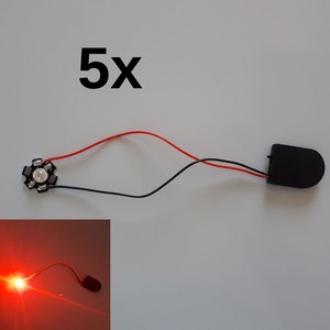 May include: A small, black LED light module with red and black wires connected to a black battery holder. The text "5x" is above the light module. A smaller image shows the LED emitting red light.