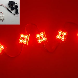 May include: Red LED light modules connected in a series, with a power supply and on/off switch. Each module contains four bright LED lights. The background is a solid red color.