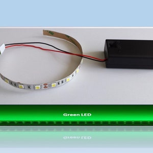 Könnte beinhalten: Ein weißer LED-Lichtstreifen mit einem schwarzen Batteriepack und roten und schwarzen Kabeln. Der LED-Streifen ist zu einem Kreis geformt. Der Text "Green LED" ist unter dem Bild sichtbar.