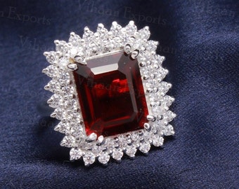 May include: A silver ring with a large, rectangular, red gemstone surrounded by a double row of smaller, clear gemstones.