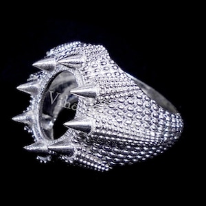 May include: Silver ring with a large, round, open setting and a textured band. The band is covered in small, raised dots and has a row of sharp, pointed spikes around the setting.
