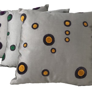 May include: Three grey throw pillows with black outlines and colourful circles. The circles are filled with yellow, green and purple.