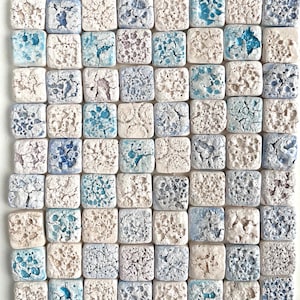 May include: A collection of small, square ceramic tiles arranged in a grid pattern. The tiles feature a textured, crackled surface with variations of white, blue, and purple hues. The overall effect is a mosaic-like appearance.