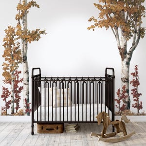 May include: A black metal cot with a white mattress and a white and brown patterned pillow. A wooden rocking horse is in the foreground. The background features a wall mural of birch trees with autumn foliage.