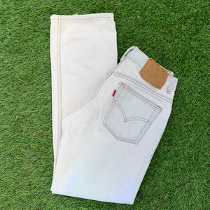 May include: A pair of light-wash denim jeans with a brown leather patch on the back pocket. The jeans have a straight leg and a relaxed fit.