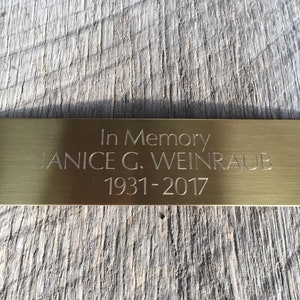 May include: A gold-colored metal plaque with the inscription "In Memory Janice G. Weinraub 1931-2017".