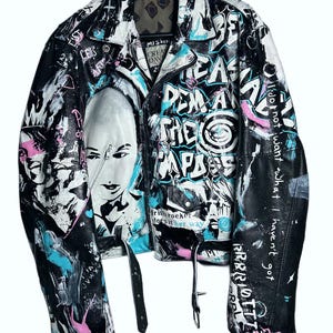 May include: Black leather jacket with graffiti-style artwork in white, blue, and pink. Features a portrait and text including "REMA THE PARADE" and "I do not want what I haven't got". Includes a belt and silver hardware.