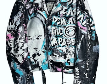 Könnte beinhalten: Schwarze Lederjacke mit Graffiti-Kunst in Weiß, Blau und Rosa. Mit einem Porträt und Text, darunter "REMA THE PARADE" und "I do not want what I haven't got". Enthält einen Gürtel und silberfarbene Hardware.
