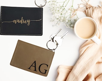 May include: Two personalized leather keychains. One is black with the name "audrey" in gold lettering. The other is brown with the initials "AG" in black lettering.