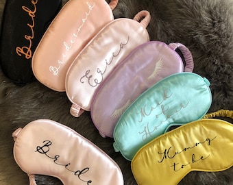 May include: An assortment of satin sleep masks in various colors, including black, pink, lavender, and yellow. Each mask features text such as "Bride," "Bridesmaid," and "Mummy to be." The masks have elastic bands and are designed for eye coverage.