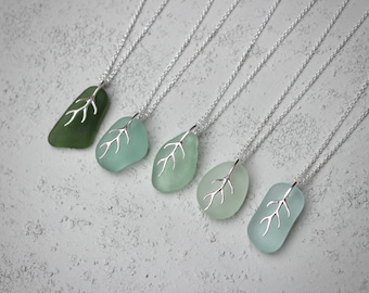 May include: Five silver necklaces with sea glass pendants. Each pendant features a silver tree branch design. The sea glass is in shades of green and blue.