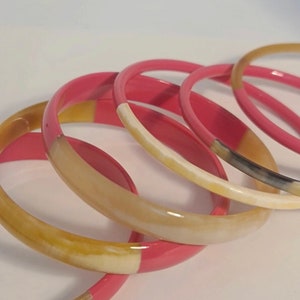 Può includere: Set di sei braccialetti in un'alternanza di rosa e crema. I braccialetti sono realizzati in corno e hanno una finitura lucida.
