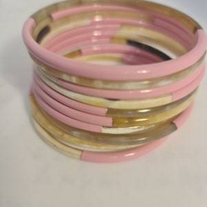 Peut inclure: Une pile de bracelets roses et bruns. Les bracelets sont en corne et ont une finition brillante.