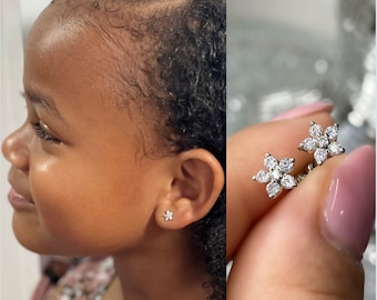 Puede incluir: Un par de pendientes de plata en forma de flor con piedras de circonita cúbica transparentes. Los pendientes se muestran en la oreja de una persona y en una vista de cerca.