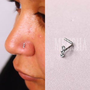 Peut inclure: Un anneau de nez argenté avec trois strass clairs alignés verticalement. L'anneau de nez est plié à un angle de 90 degrés.