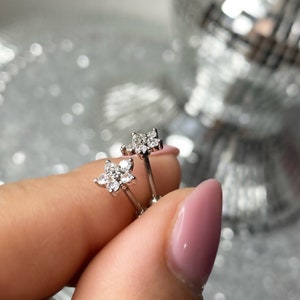 May include: A pair of silver stud earrings with a flower design featuring clear cubic zirconia stones.