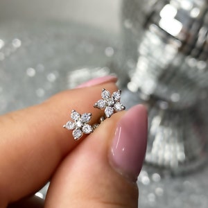 May include: A pair of silver flower-shaped stud earrings with clear cubic zirconia stones.