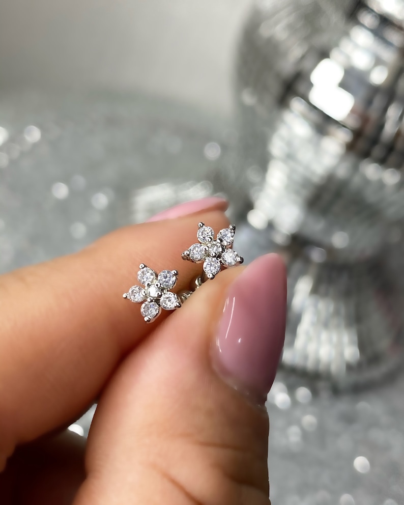 May include: A pair of silver flower-shaped stud earrings with clear cubic zirconia stones.