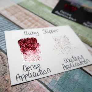May include: A close-up of two samples of red glitter, labeled "Ruby Slipper". The left sample shows a dense application of glitter, while the right sample shows a watery application.