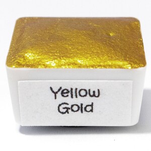 May include: A small, square pan of yellow gold watercolor paint. The pan is labeled "Yellow Gold".