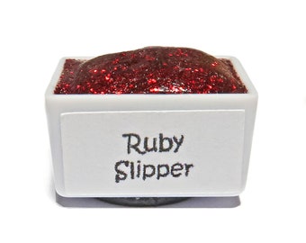 May include: A small white pan with a red glitter paint inside. The pan has a label that says "Ruby Slipper".