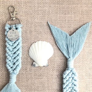 May include: A light blue macrame keychain with a silver charm that says "Seas the day". The keychain is next to a light blue macrame mermaid tail.
