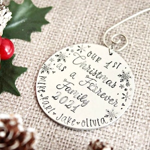 May include: Silver Christmas ornament with the text "Our 1st Christmas as a Family Forever 2021 Mike Kari Jake Olivia" and snowflake designs.