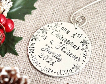 May include: Silver Christmas ornament with the text "Our 1st Christmas as a Family Forever 2021 Mike Kari Jake Olivia" and snowflake designs.