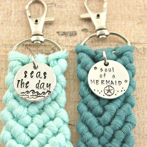 May include: Two crocheted keychains with silver charms. The keychain on the left is light blue and has a charm that says "Seas the day" with a wave design. The keychain on the right is teal and has a charm that says "Soul of a Mermaid" with a starfish design.