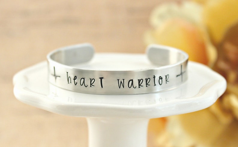 May include: Silver cuff bracelet with the words "heart warrior" and a cross on each side.