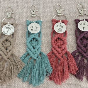 May include: Four handmade macrame keychains with personalized metal tags. The keychains are in beige, teal, red, and purple. The tags read "Kyleigh Proverbs 31:25", "ellen", "addie", and "blessed".