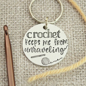 May include: Silver keychain with a round tag that says "Crochet keeps me from unraveling". The tag has a small crochet hook and ball of yarn design.