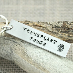 May include: Silver keychain with a heart and the text "TRANSPLANT TOUGH".