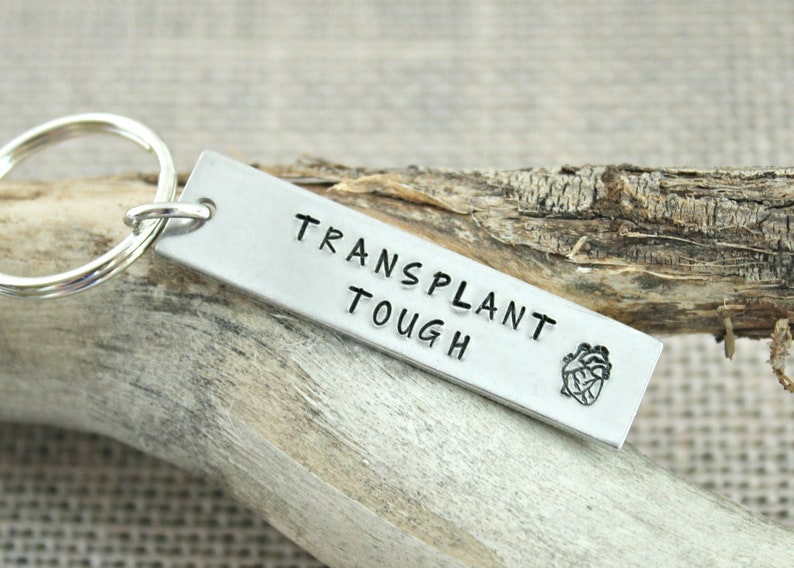 May include: Silver keychain with a heart and the text "TRANSPLANT TOUGH".