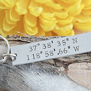 May include: Silver keychain with a rectangular tag engraved with the coordinates "37° 38' 35" N 118° 58' .66" W".