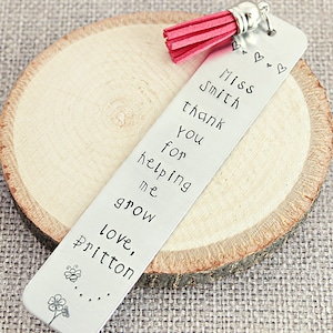 May include: Silver bookmark with a pink tassel, engraved with the text "Miss Smith thank you for helping me grow love, Pritton".