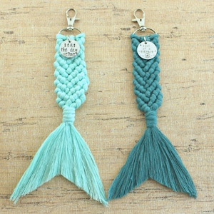 May include: Two mermaid tail keychains with silver charms. One charm says "Seas the day" and the other says "Soul of a Mermaid". The tail on the left is light blue and the tail on the right is teal.